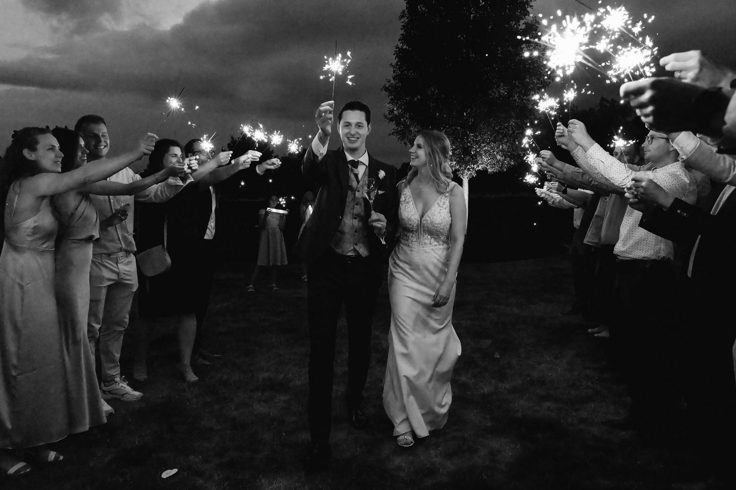 Black and white photo of newlyweds walking through sparkler send-off tunnel at night.