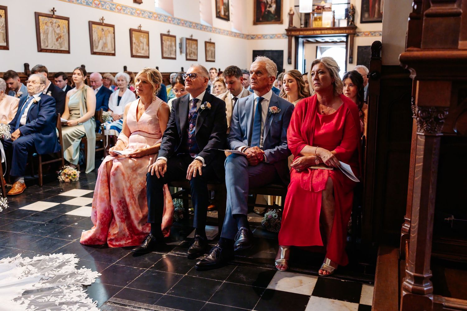 Wedding guests seated in church pews watching ceremony in formal attire.