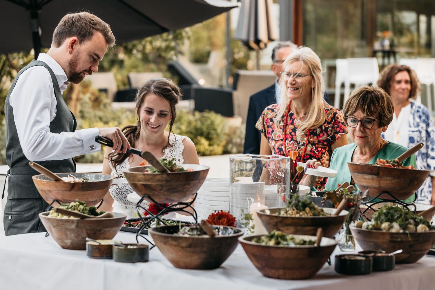 Catering staff serving fresh salads from rustic wooden bowls at an elegant outdoor event.
