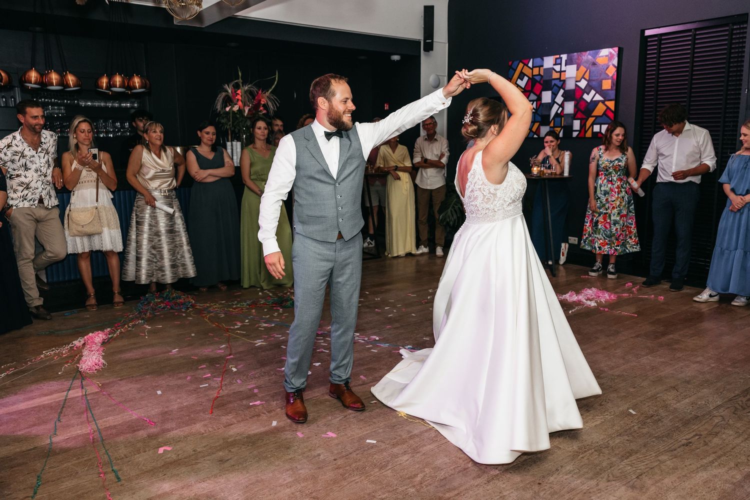 Groom spins his bride gracefully on the dance floor as wedding guests look on during the first dance celebration.