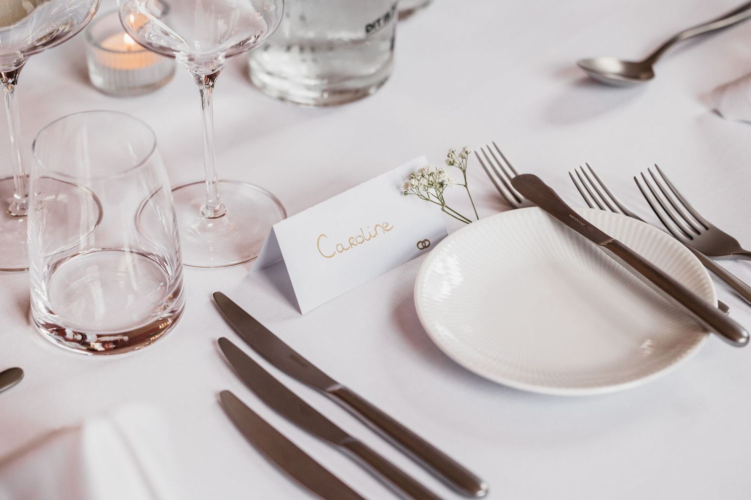 Elegant wedding table setting with white place card, crystal glasses, and baby's breath floral accent.