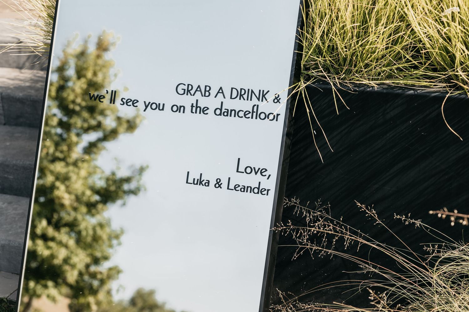 Wedding mirror sign reading Grab a Drink and see you on the dancefloor, Love Luka and Leander.