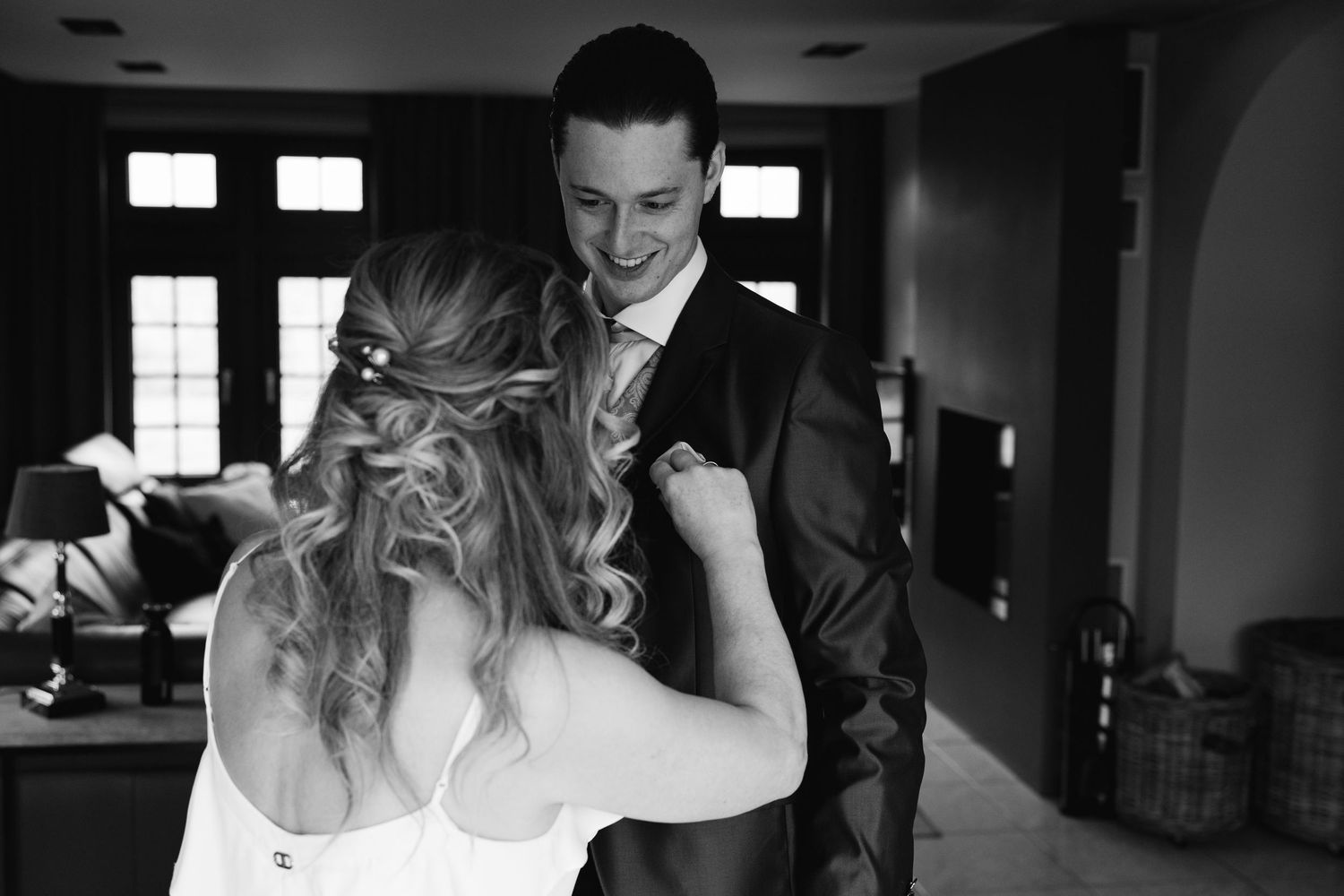 Black and white photo of bride fixing groom's lapel while he smiles warmly.