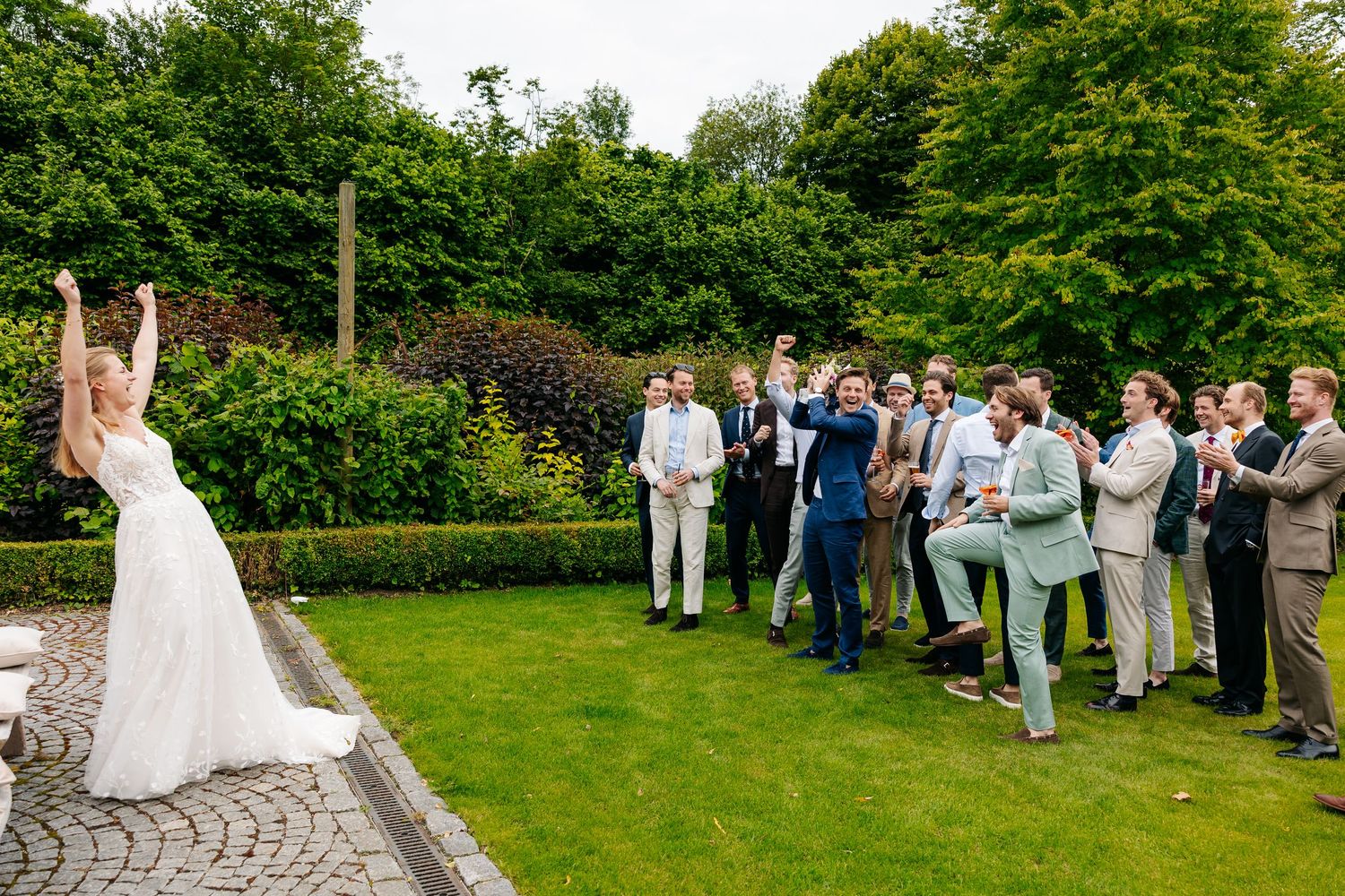Bride tossing bouquet to a group of groomsmen in a lush garden setting.