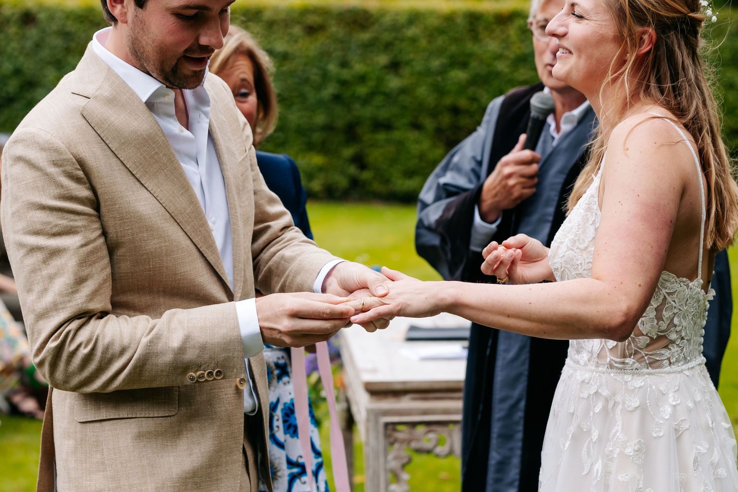 Groom places wedding ring on bride's finger during an outdoor ceremony.