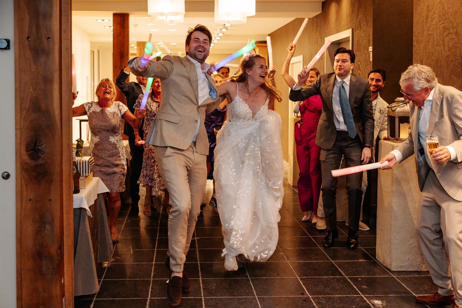 Bride in lace gown and groom entering wedding reception to cheering guests holding light-up accessories.