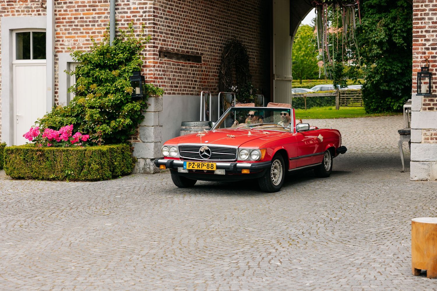 Classic red Mercedes-Benz convertible driving through brick archway at historic venue.