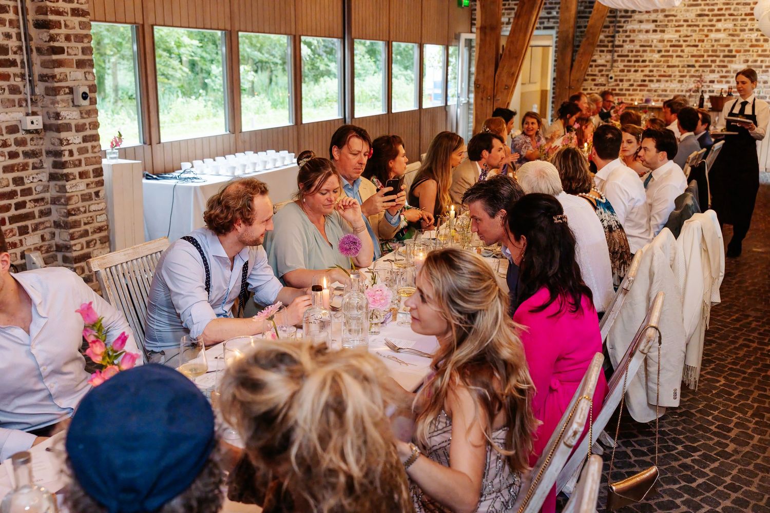 Guests seated at decorated tables during a wedding reception dinner in a rustic brick venue.