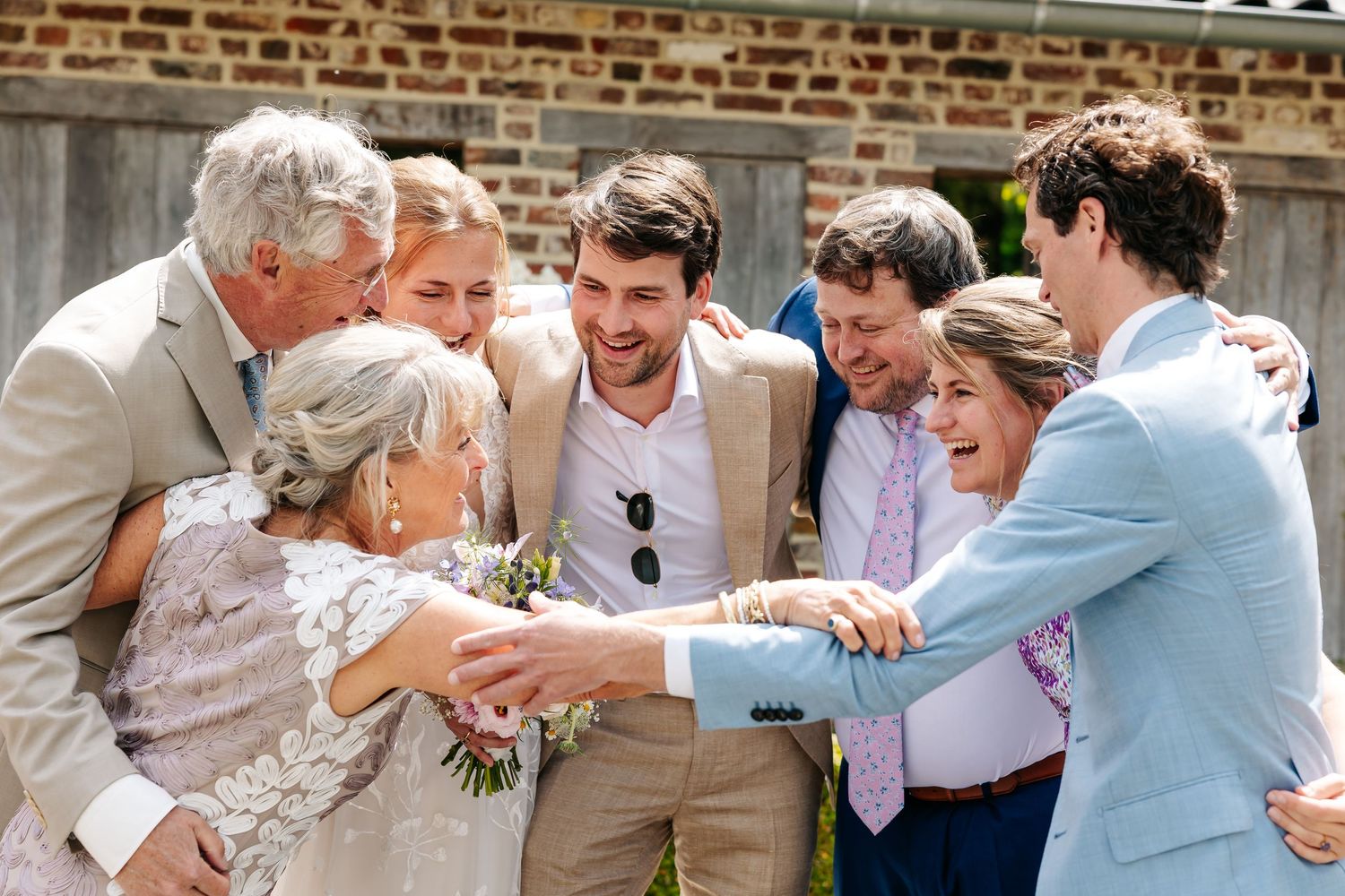 Joyful wedding group hug with bride, groom and family celebrating outdoors in summer.