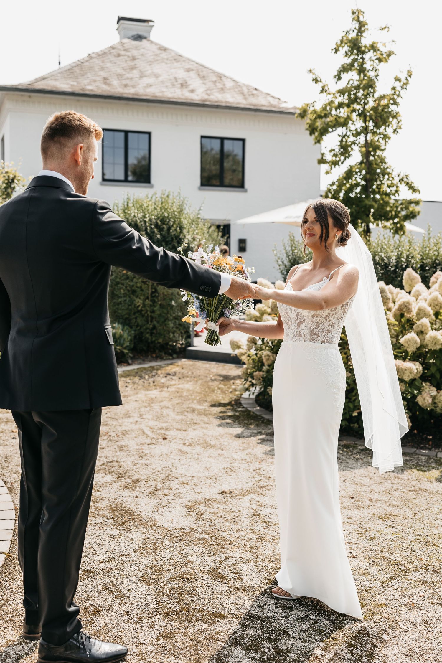 Groom presents colorful bridal bouquet to bride during outdoor first look ceremony.