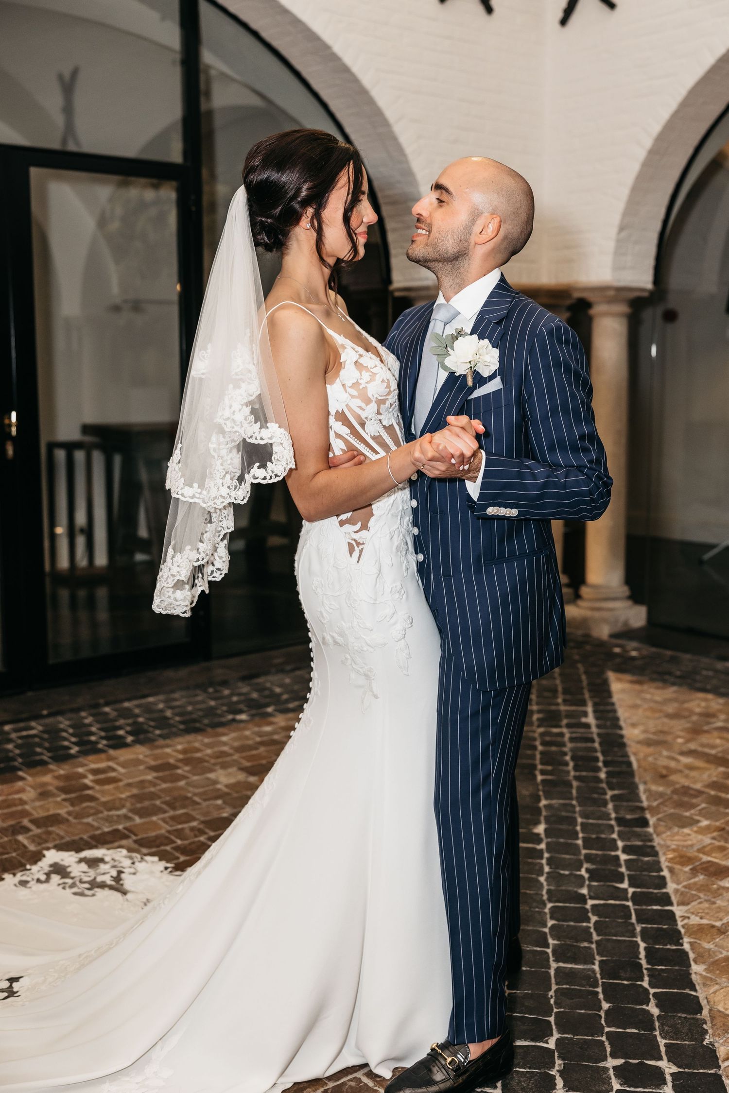 Bride in lace wedding dress and veil shares first dance with bald groom in pinstripe suit.