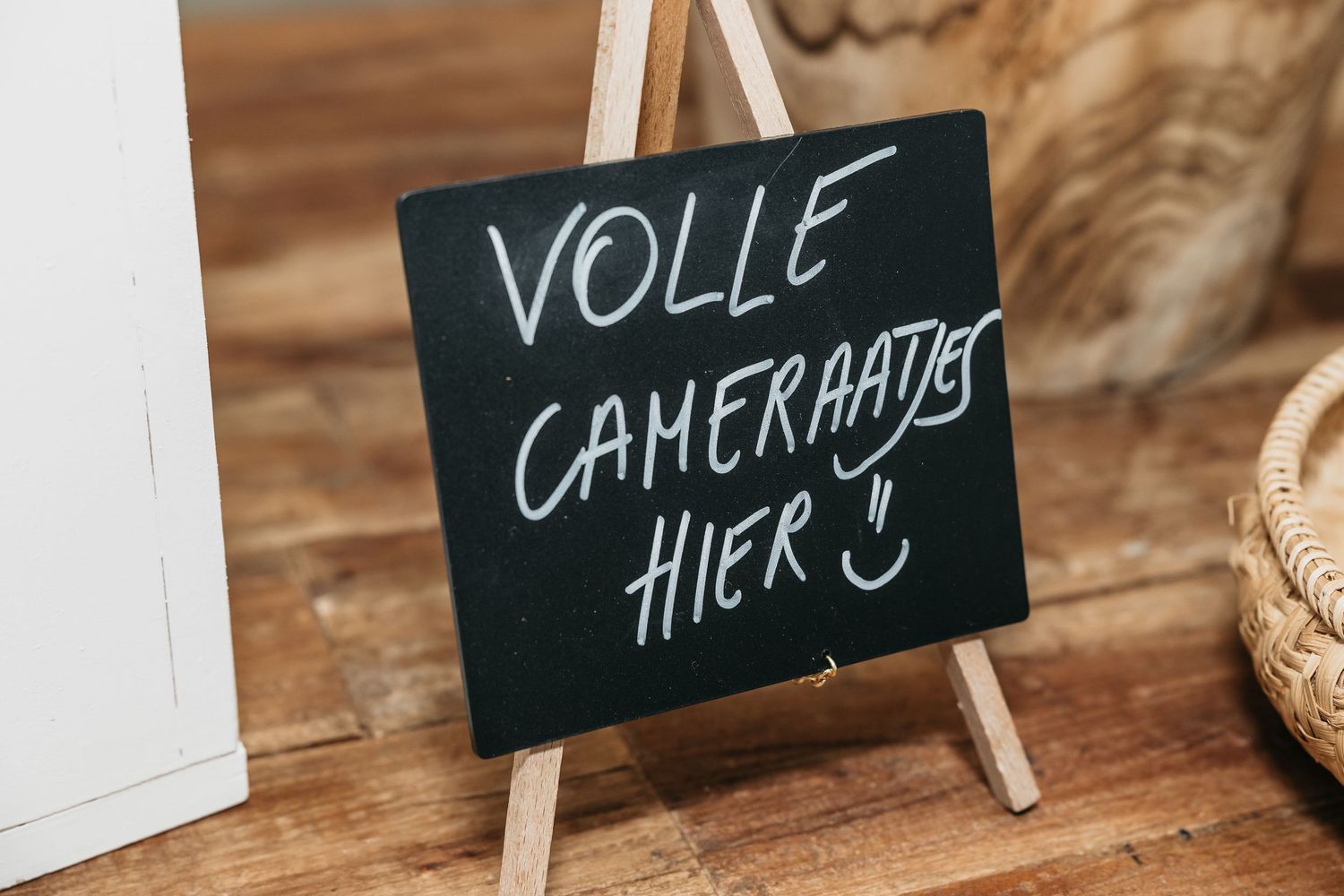 Chalkboard sign on easel reading Volle Cameraatjes Hier at wedding reception.