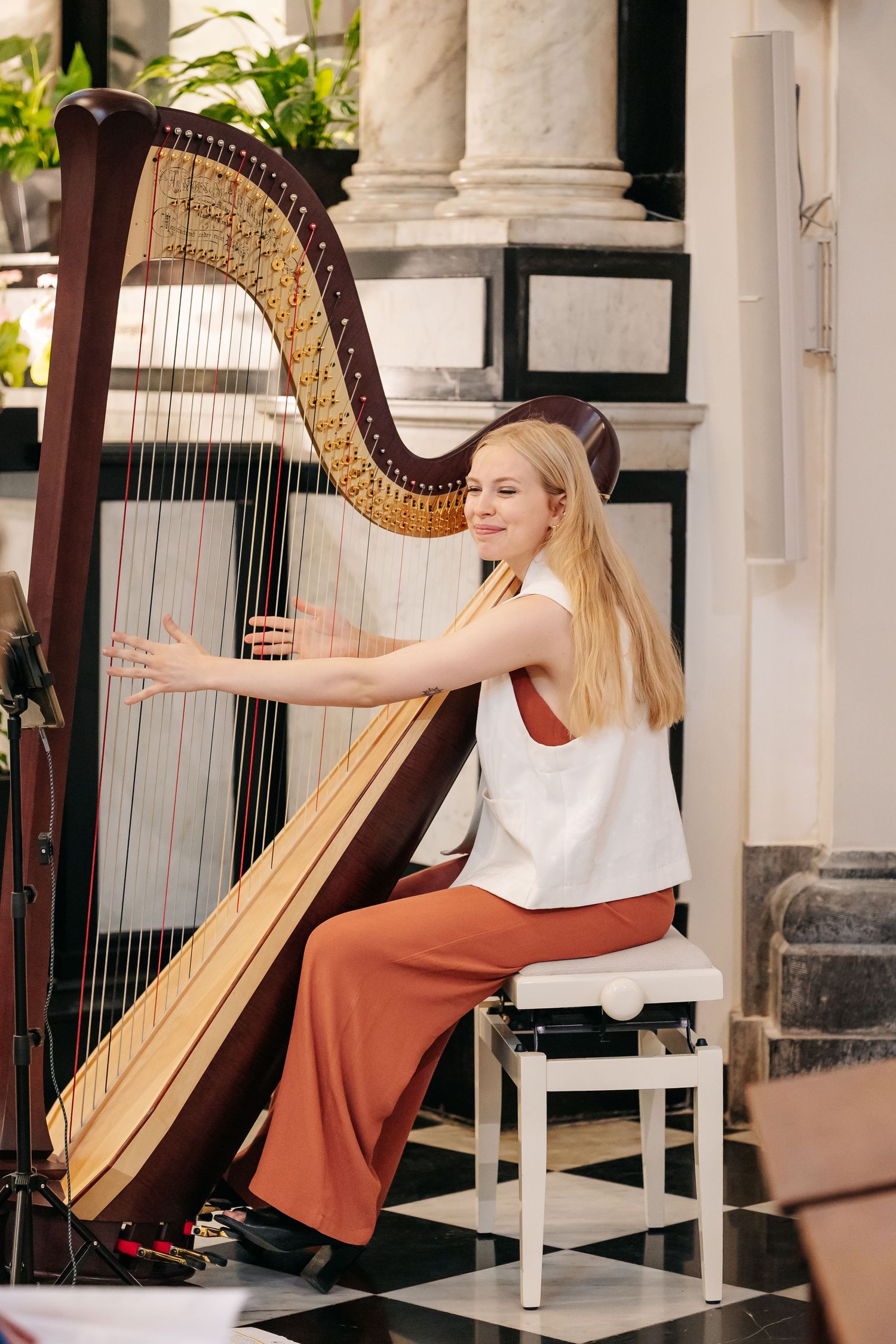 Blonde female harpist in white top performs during wedding ceremony in ornate church.