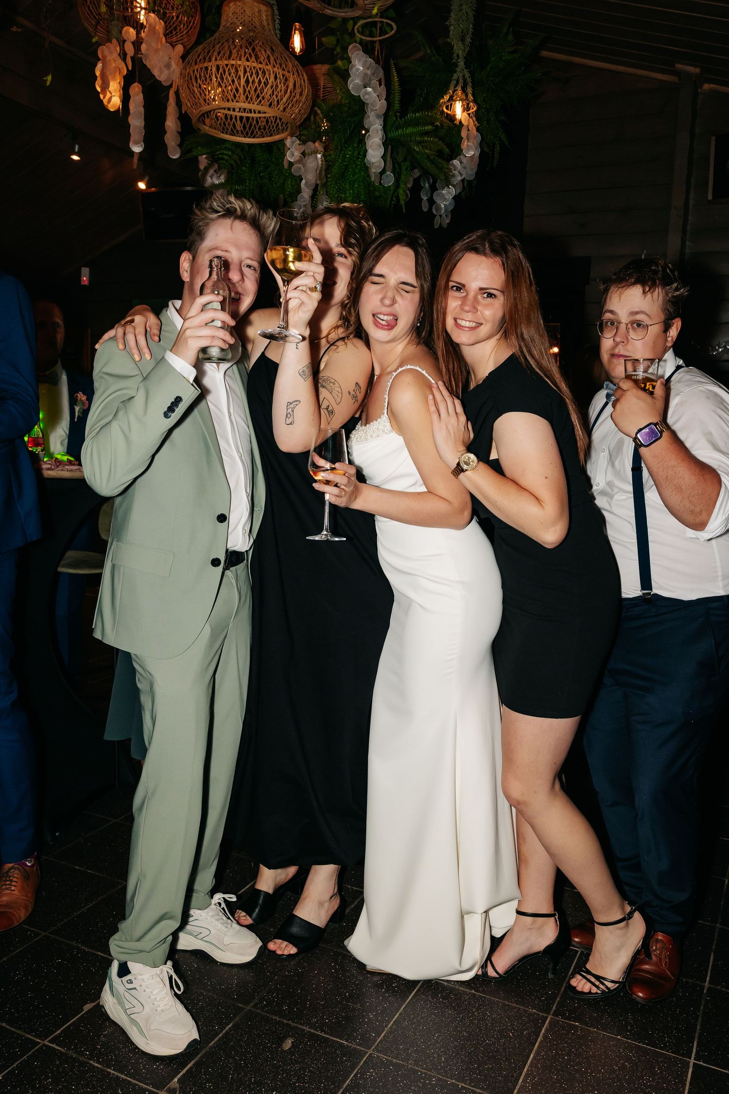 Bride poses with wedding guests holding champagne glasses at reception.