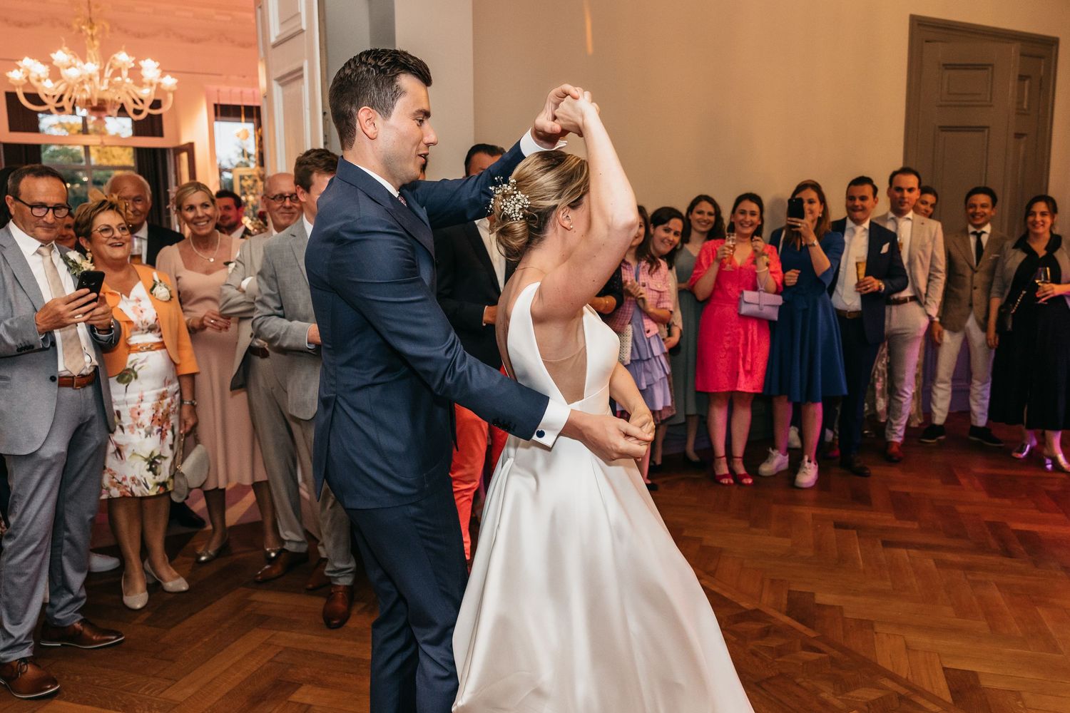 Groom twirling bride in white dress during elegant first dance at wedding reception.