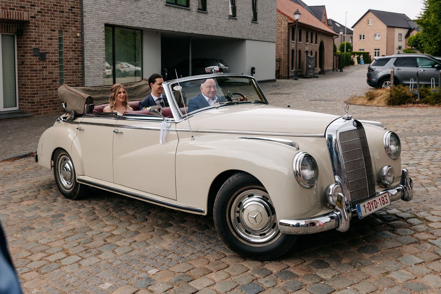Bride and groom arrive in a classic cream vintage Mercedes convertible on cobblestone street.