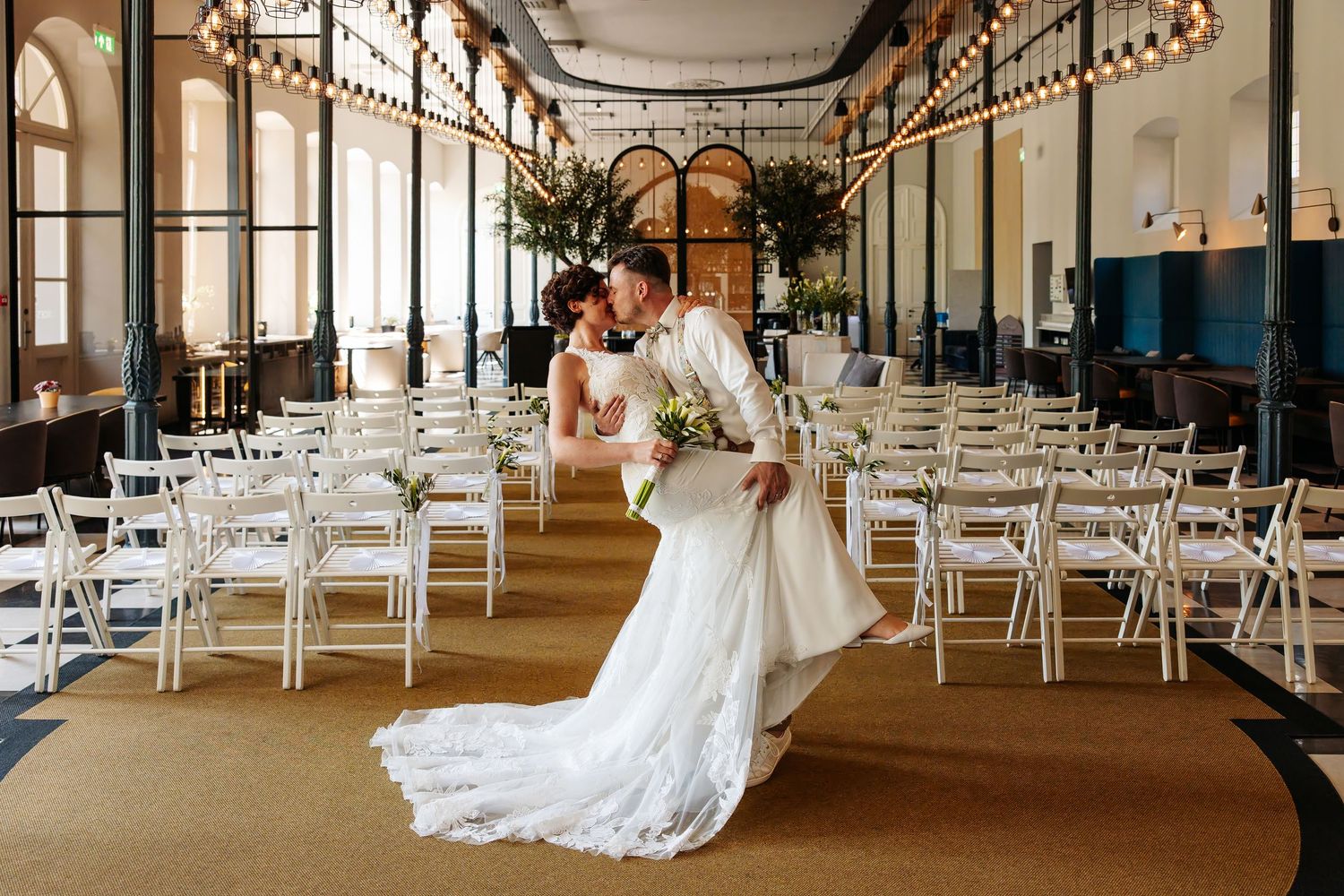 Bride and groom share romantic dip kiss in elegant chandelier ceremony venue.