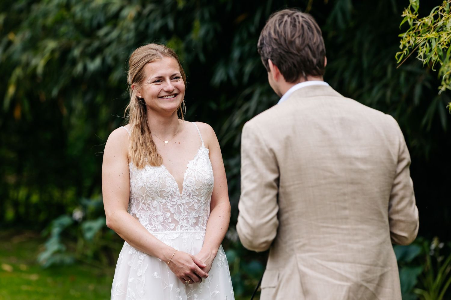 Radiant bride in lace gown smiling joyfully at groom during outdoor wedding ceremony.