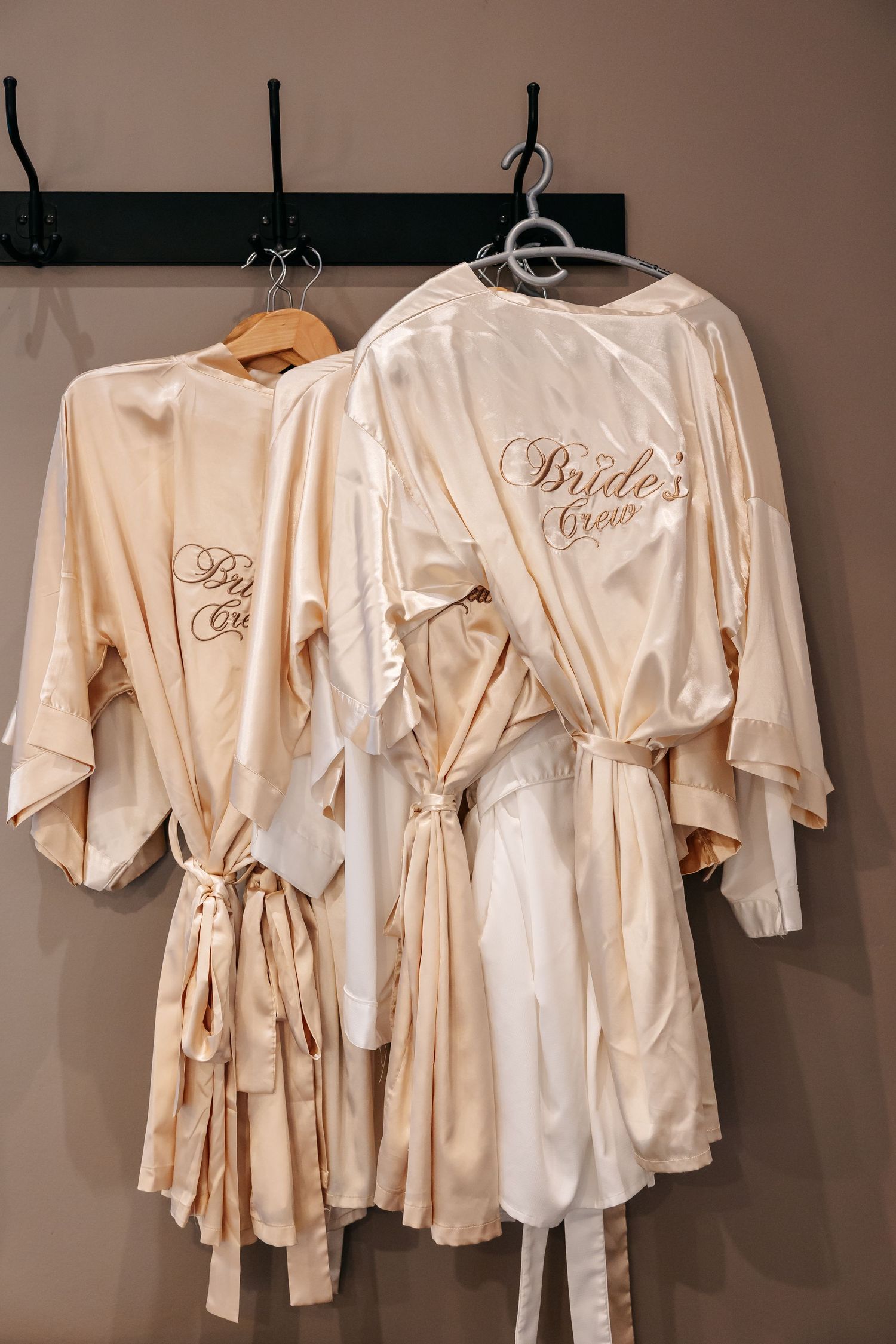 Satin bridal robes labeled Bride Crew hanging on hooks, perfect for wedding party getting-ready photos.
