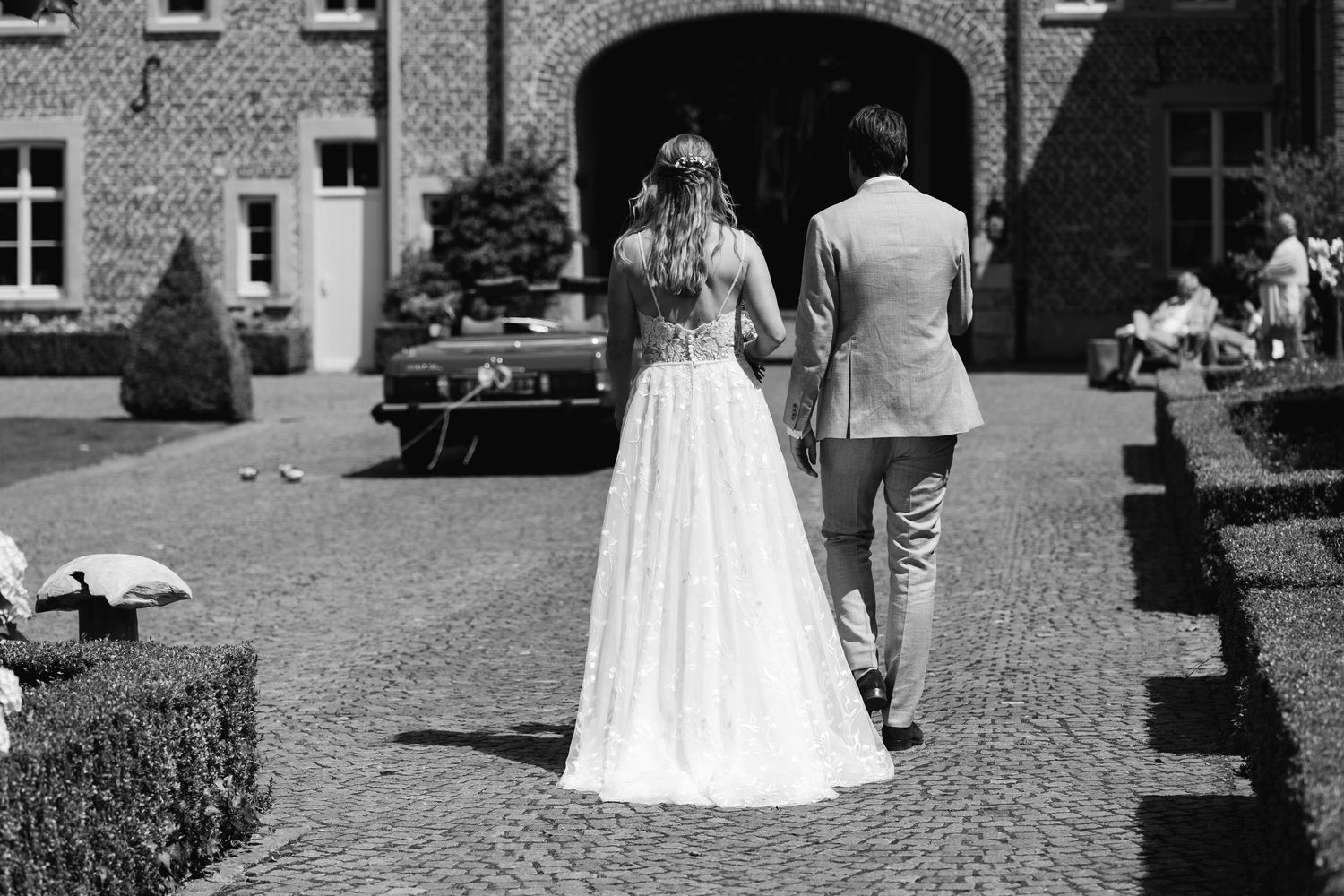 Bride and groom walking hand in hand toward elegant venue in black and white wedding photo.