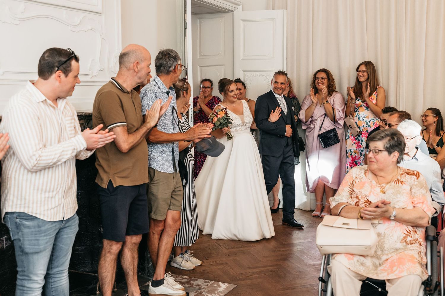 Bride and escort walking through applauding wedding guests in a bright elegant indoor venue.