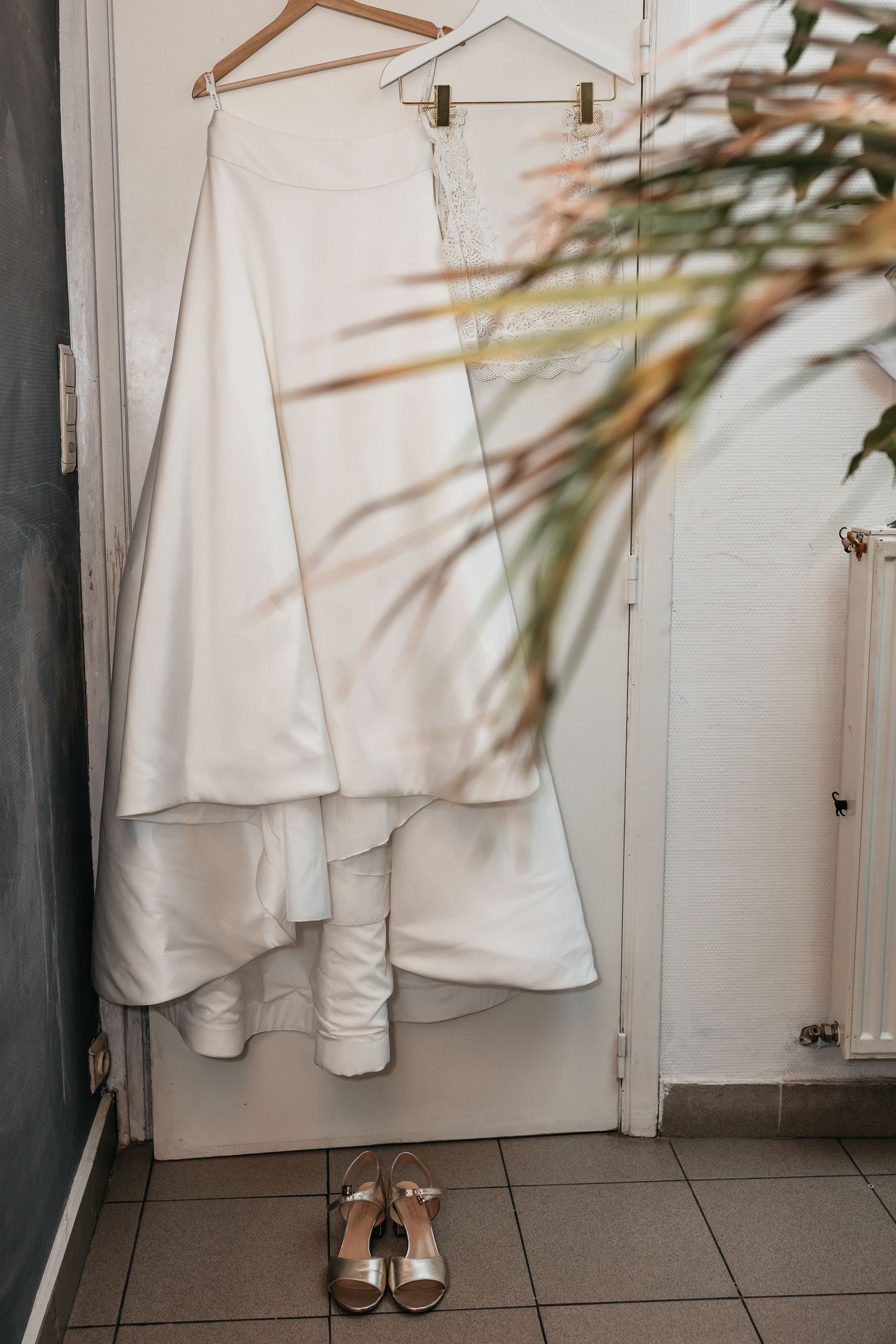 White wedding gown with lace detail hanging on door with gold bridal heels below.