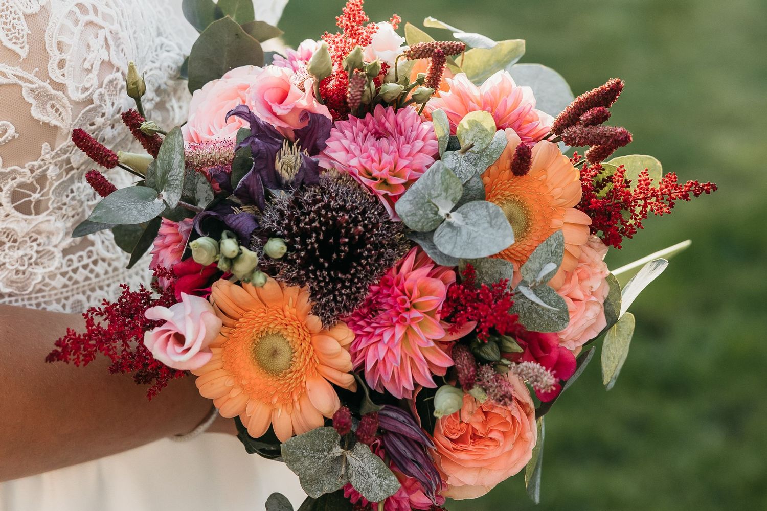 Colorful bridal bouquet with orange gerbera, pink roses, and burgundy flowers.