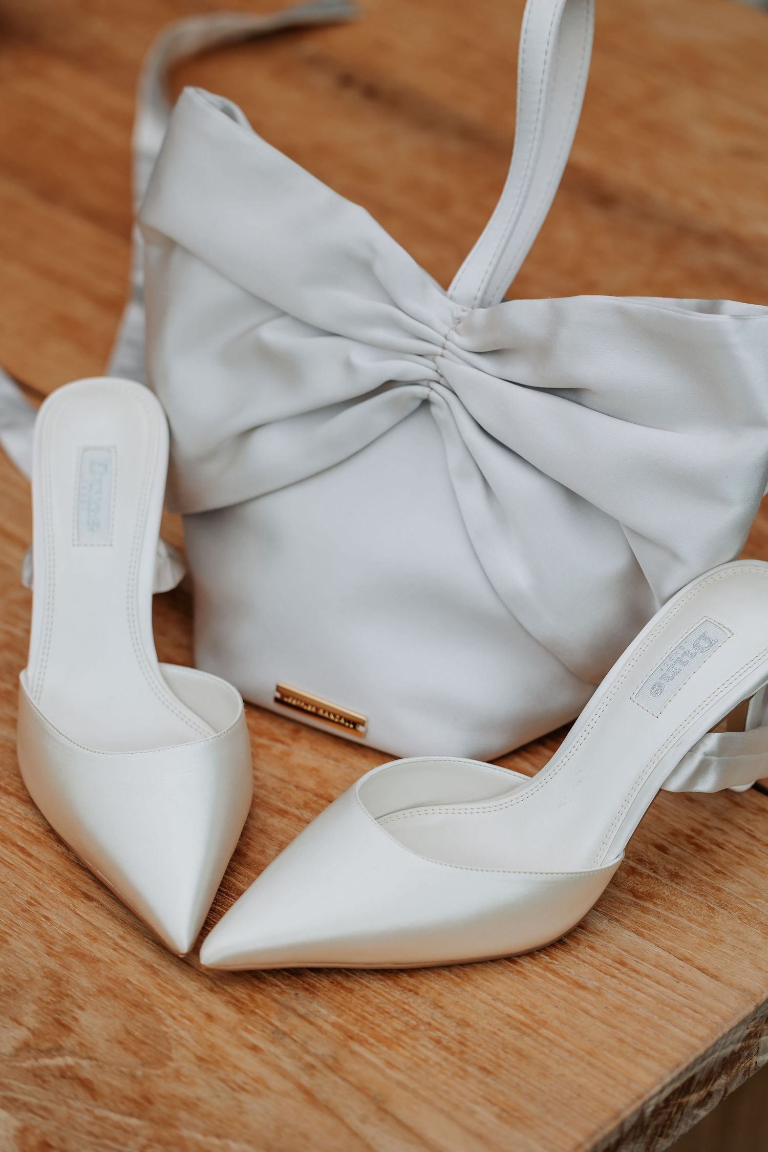 White bridal heels and matching bow clutch bag displayed on a wooden surface.