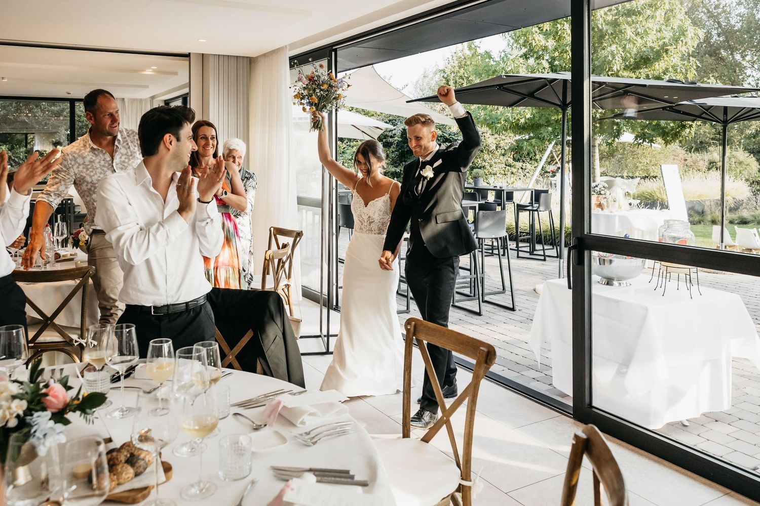 Bride and groom make a grand entrance into the wedding reception as guests cheer and applaud.