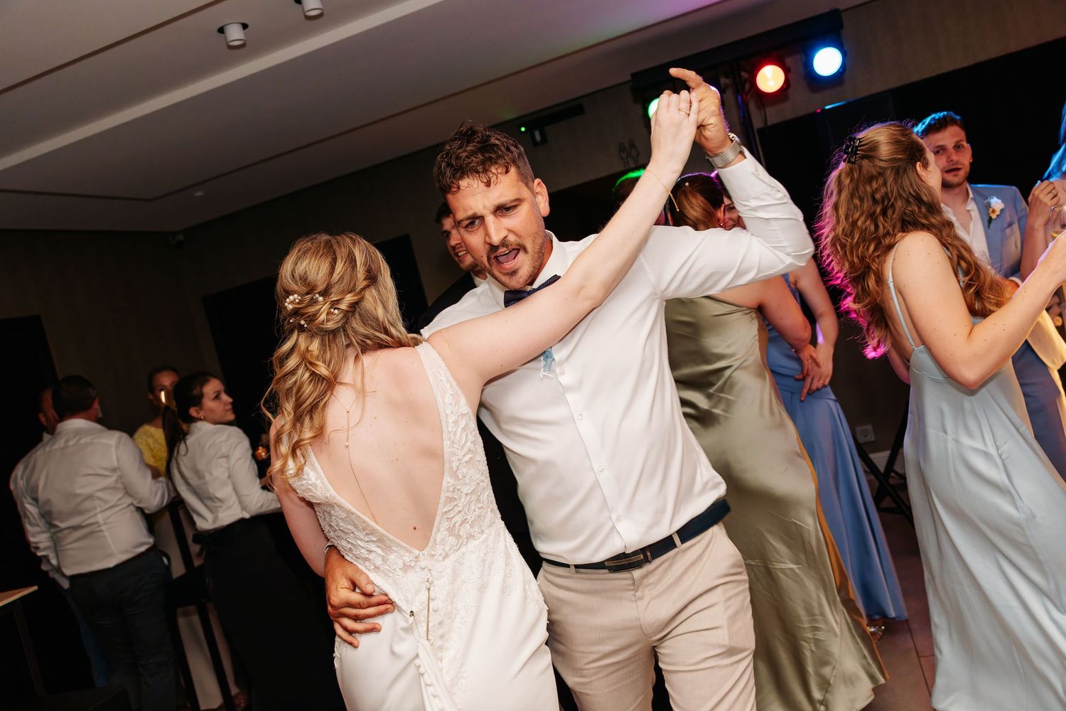 Smiling groom dances energetically with bride in backless wedding dress at reception.