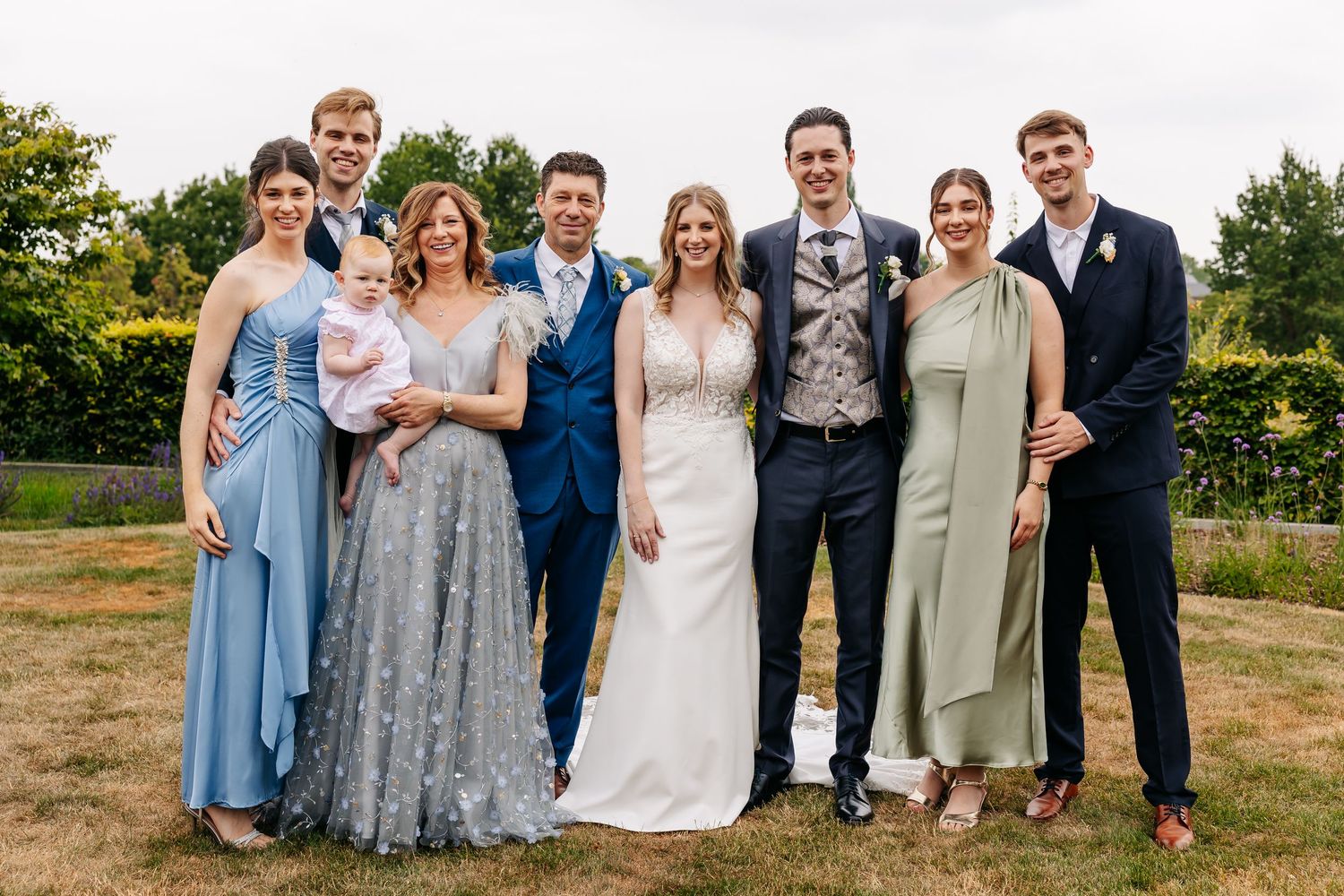 Wedding party group portrait with bride, groom and family members outdoors.