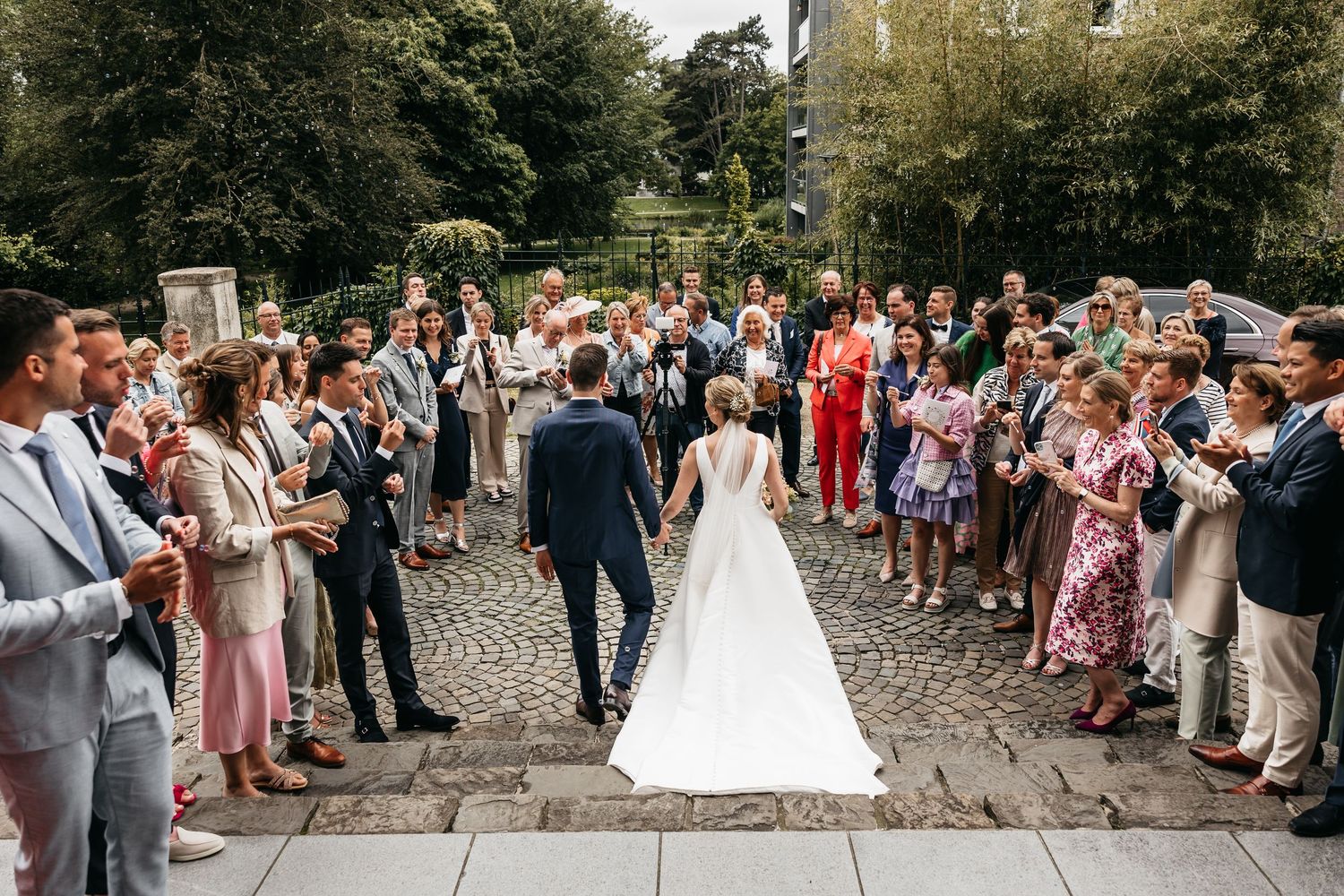 Bride and groom hold hands as guests line up to celebrate outside.