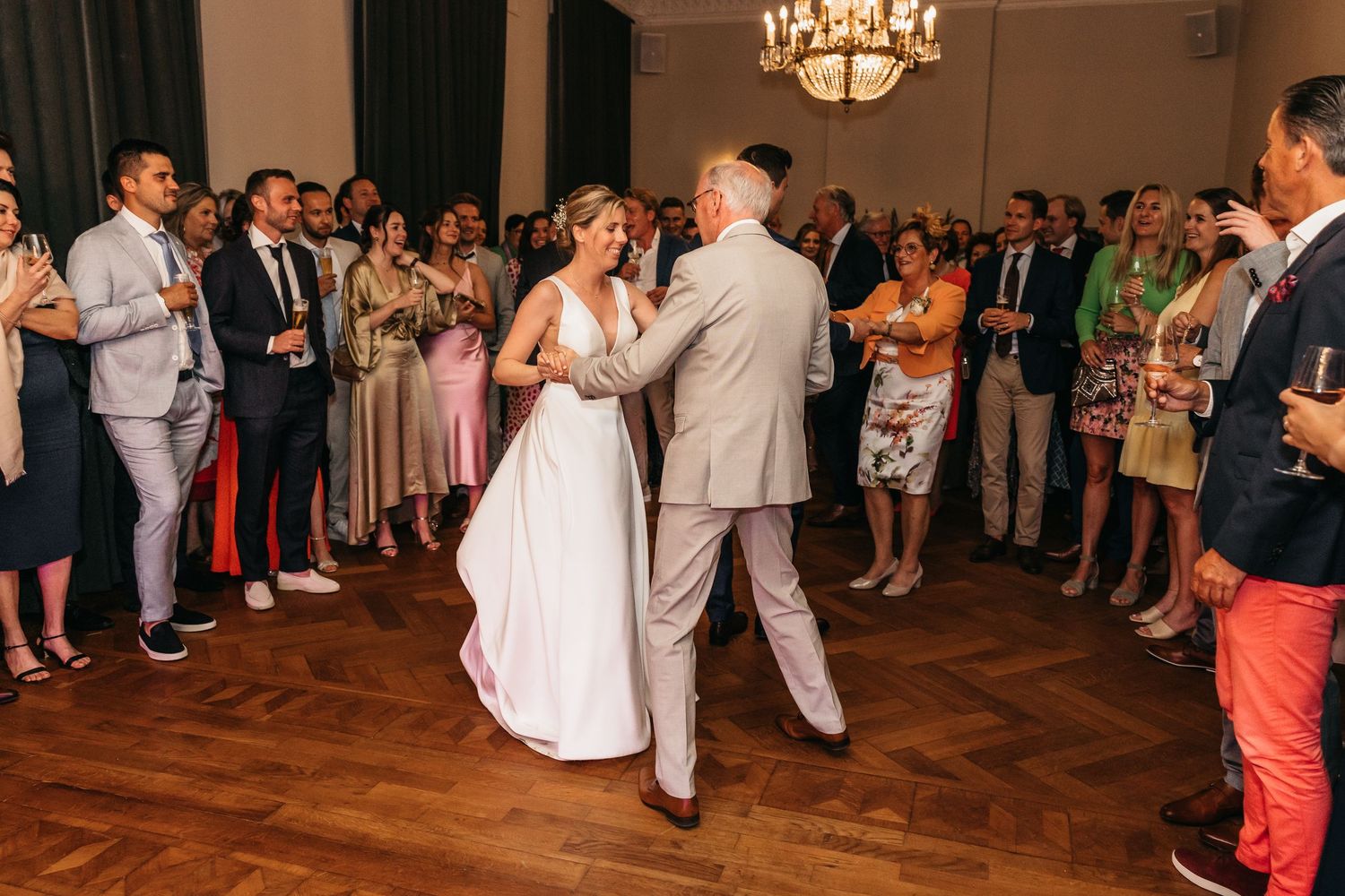 Bride in white gown shares emotional dance with father in grey suit at wedding reception.