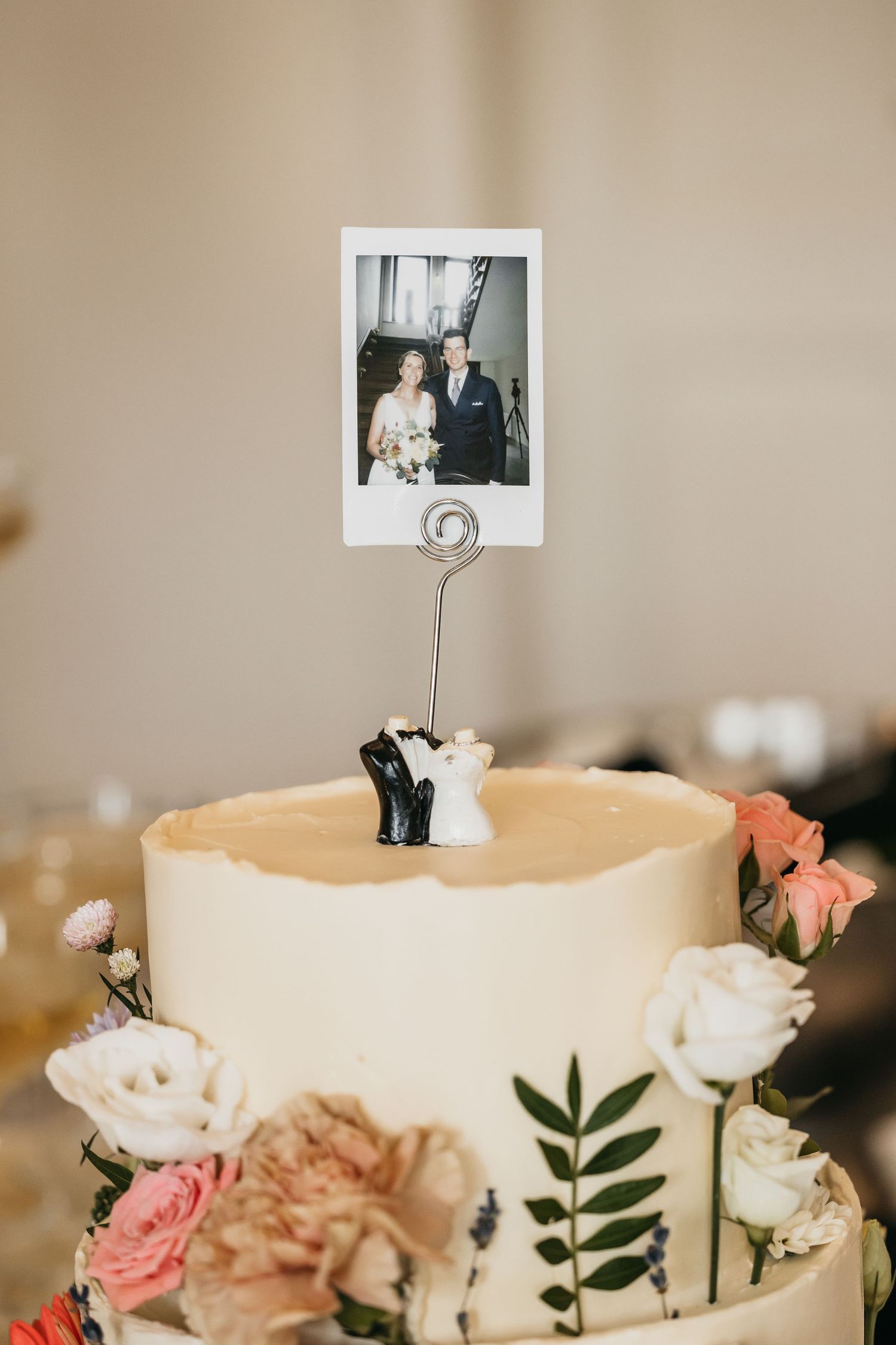 Close-up of wedding cake topper featuring bride and groom figurines with a Polaroid photo holder.