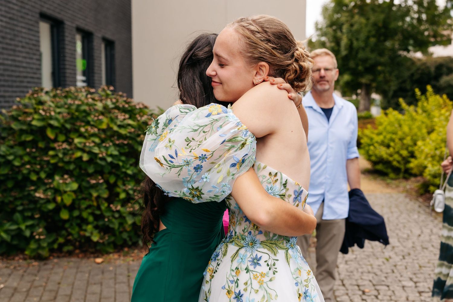 Two women share a warm embrace outdoors at a wedding celebration.