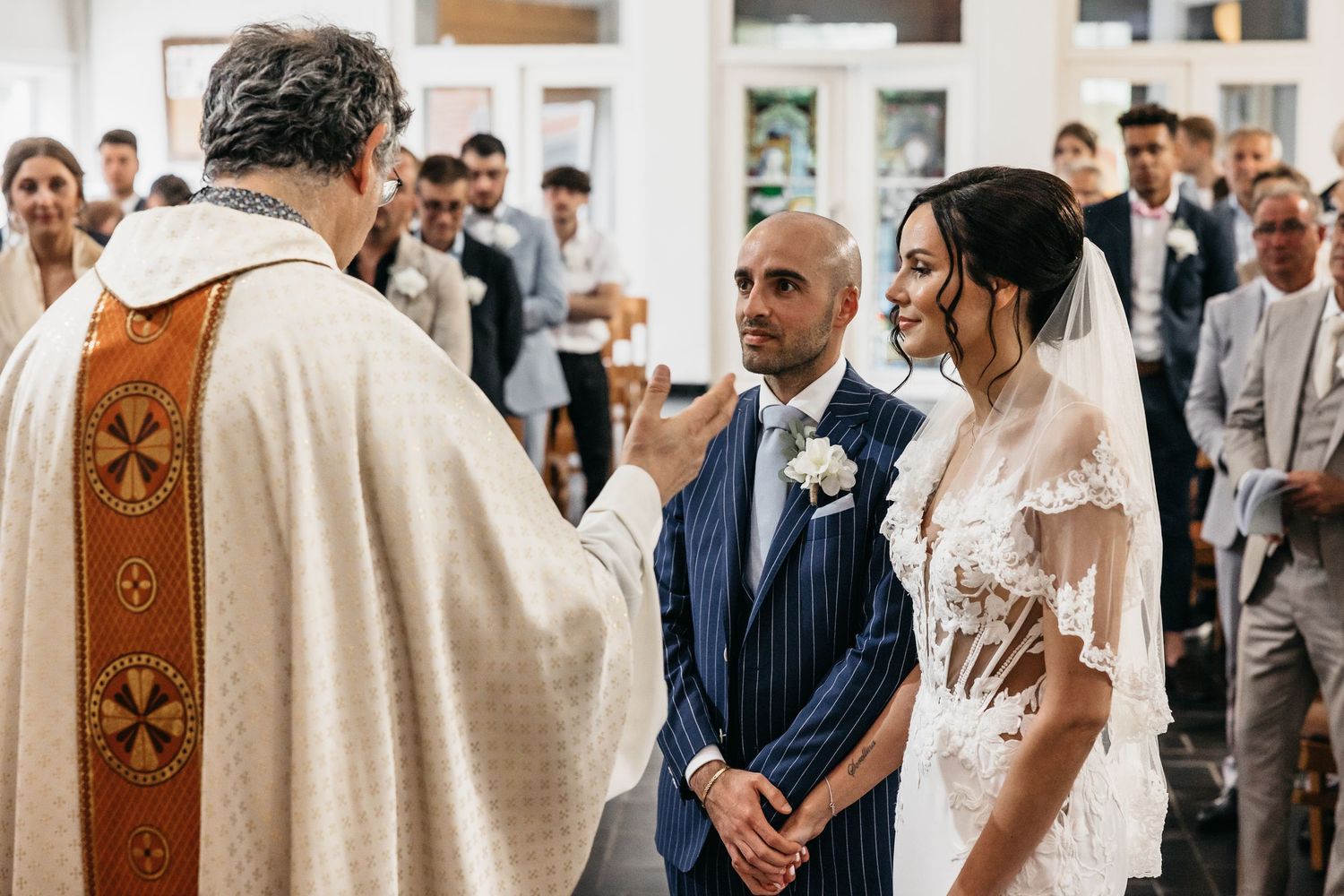 Priest blesses smiling bride and groom during a traditional church wedding ceremony.