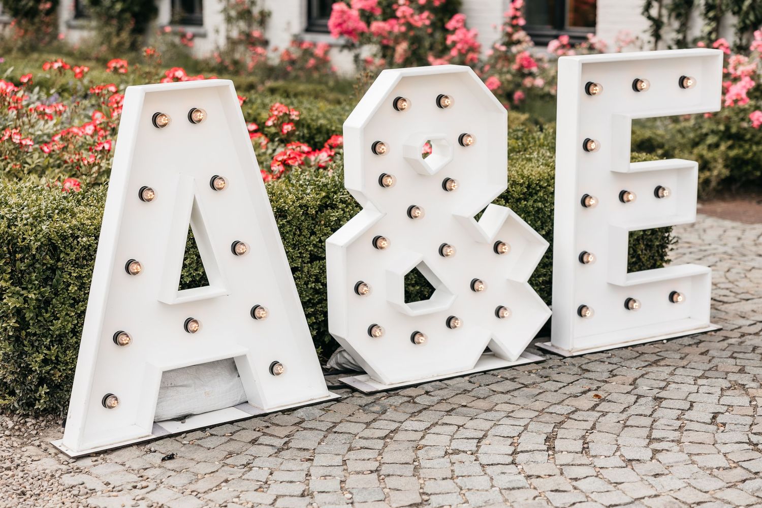 Large decorative white marquee light-up letters spelling A&E displayed on cobblestone patio.