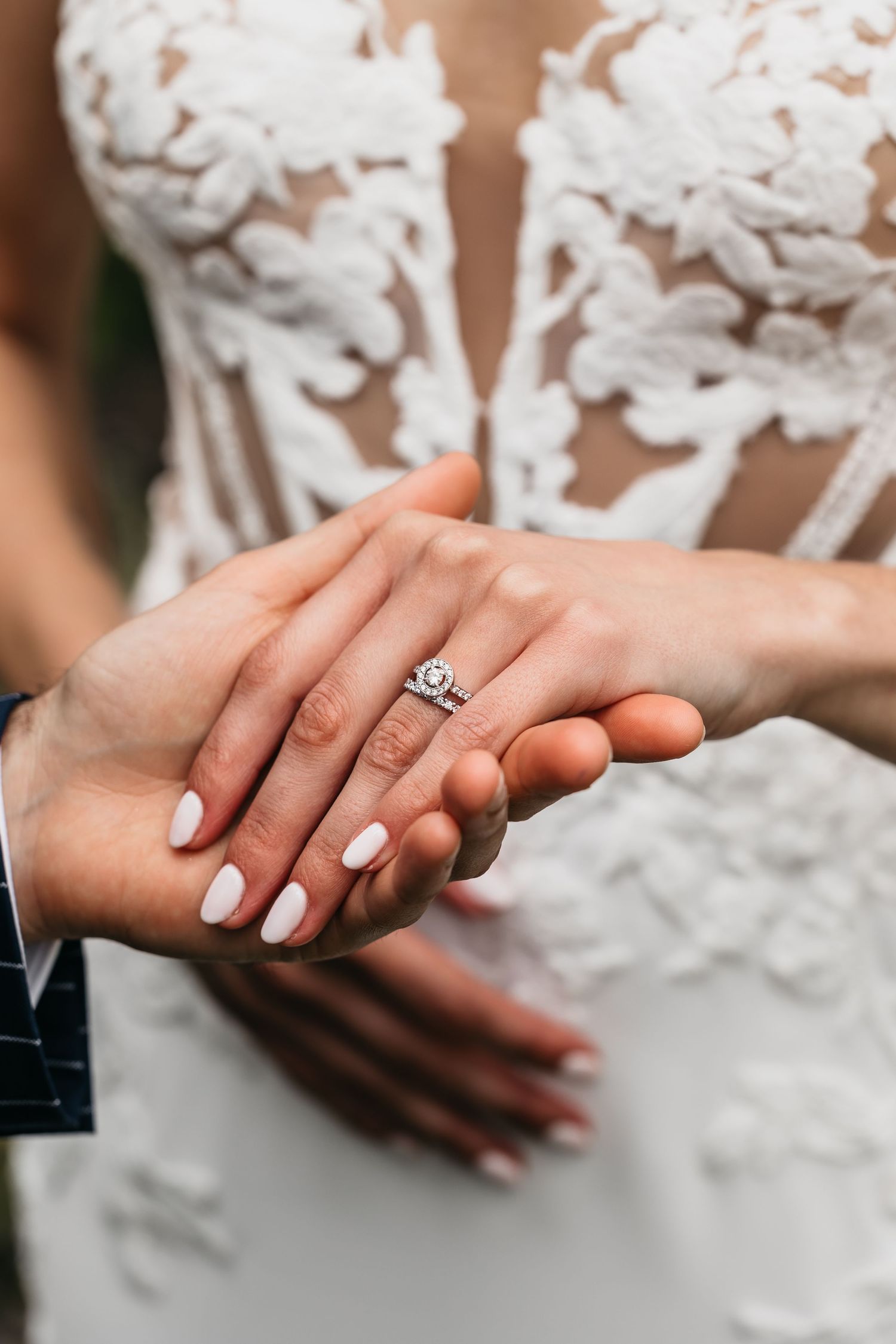 Close-up of bride's hand showing elegant diamond engagement ring with white manicure on wedding day.