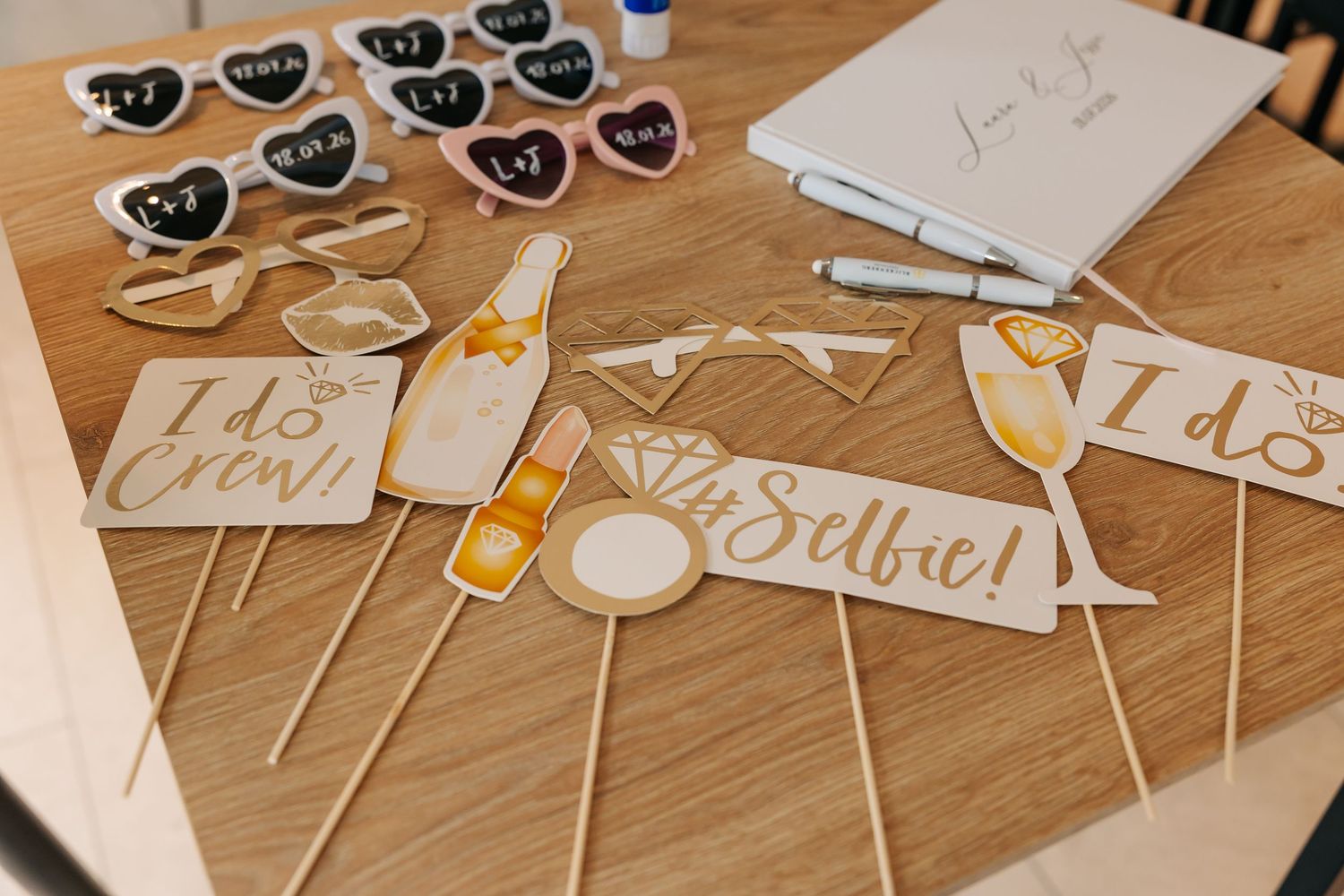 Wedding photo booth props and heart-shaped sunglasses displayed on wooden table.