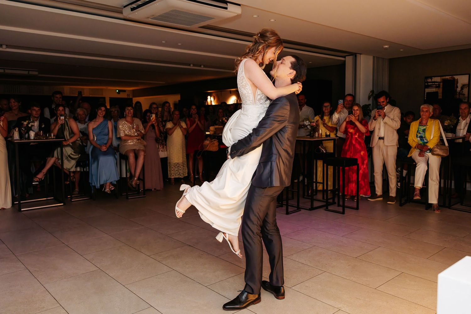 Groom lifts bride joyfully during their first dance at a wedding reception.