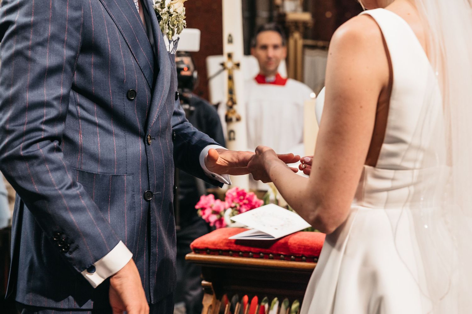 Couple exchanges rings at altar with smiling officiant in background.