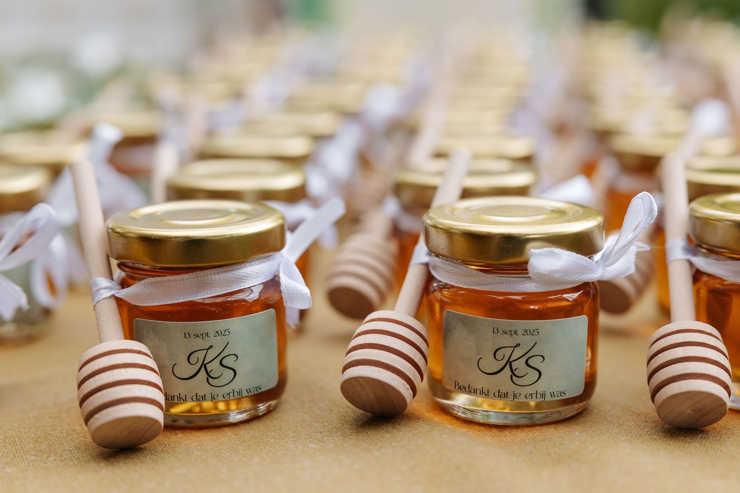 Rows of small honey jars with gold lids and wooden dippers as wedding favor gifts.