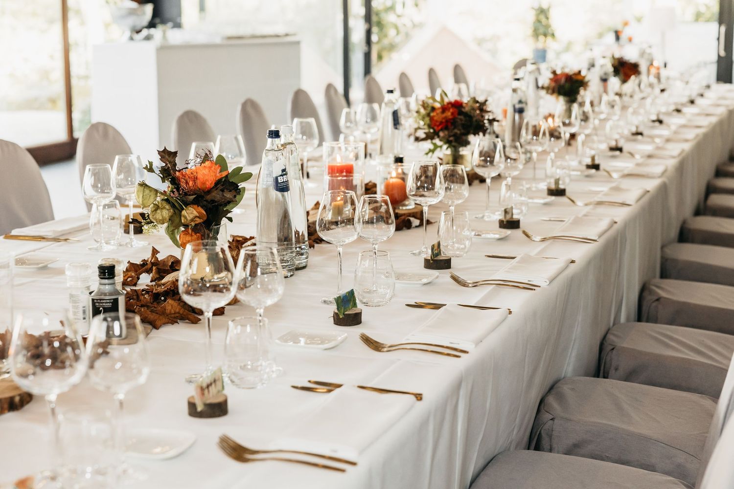 Long wedding reception table with colorful autumn floral centerpieces and glassware.