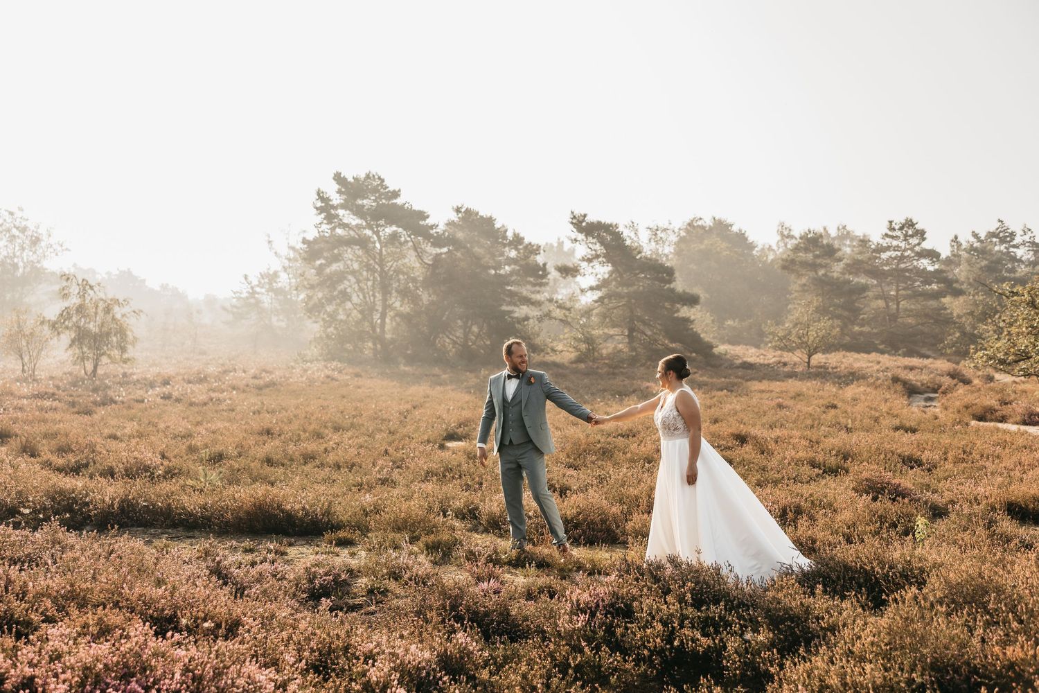 Bride and groom holding hands walking through misty golden heather fields on their wedding day.