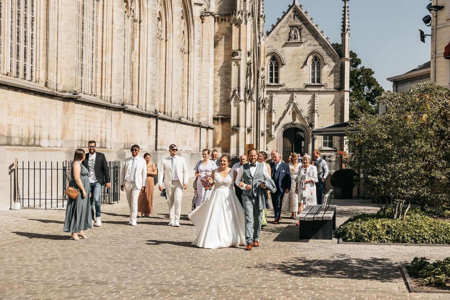 Wedding party walking together past a historic Gothic church on a sunny day after the ceremony.