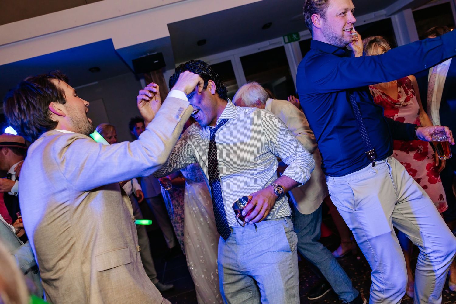 Energetic wedding guests dancing and celebrating on the dance floor under colorful party lights.