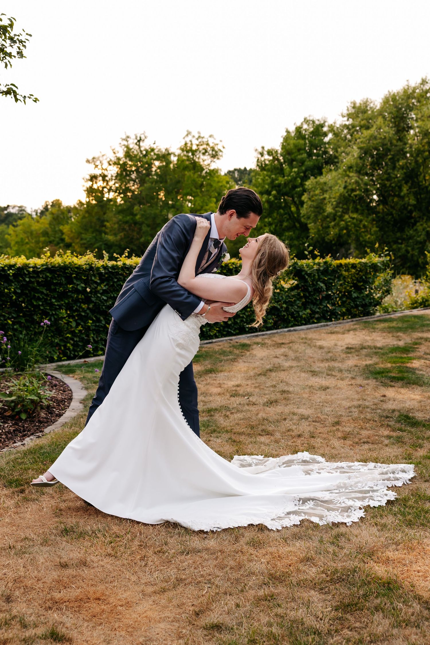 Bride and groom share a romantic dip kiss in a lush garden during their outdoor wedding ceremony.