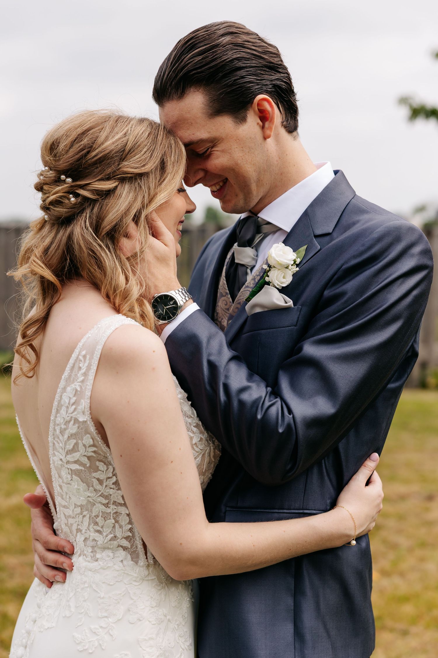 Close-up of smiling bride and groom touching foreheads, groom wearing navy suit with white boutonniere.