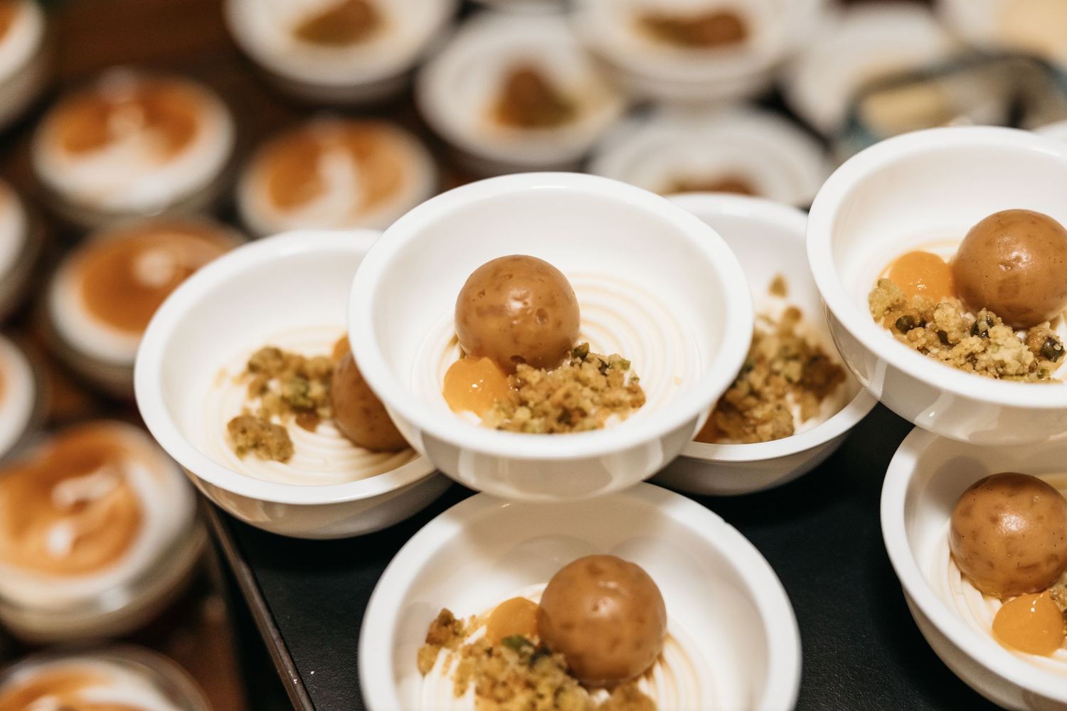 Caramel truffle balls with crushed nut topping served in white mini dishes at a wedding catering event.