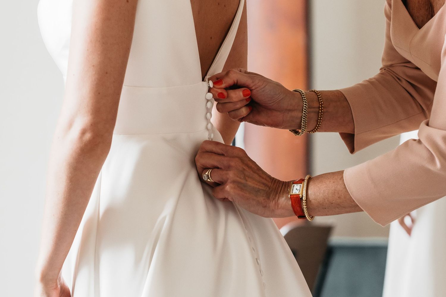 Close-up of hands fastening buttons on back of elegant white wedding dress.
